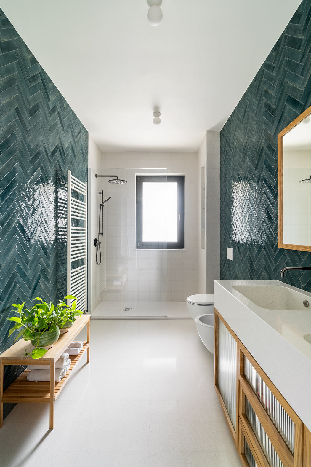A modern bathroom with green herringbone tile walls, a white vanity, and a large window.