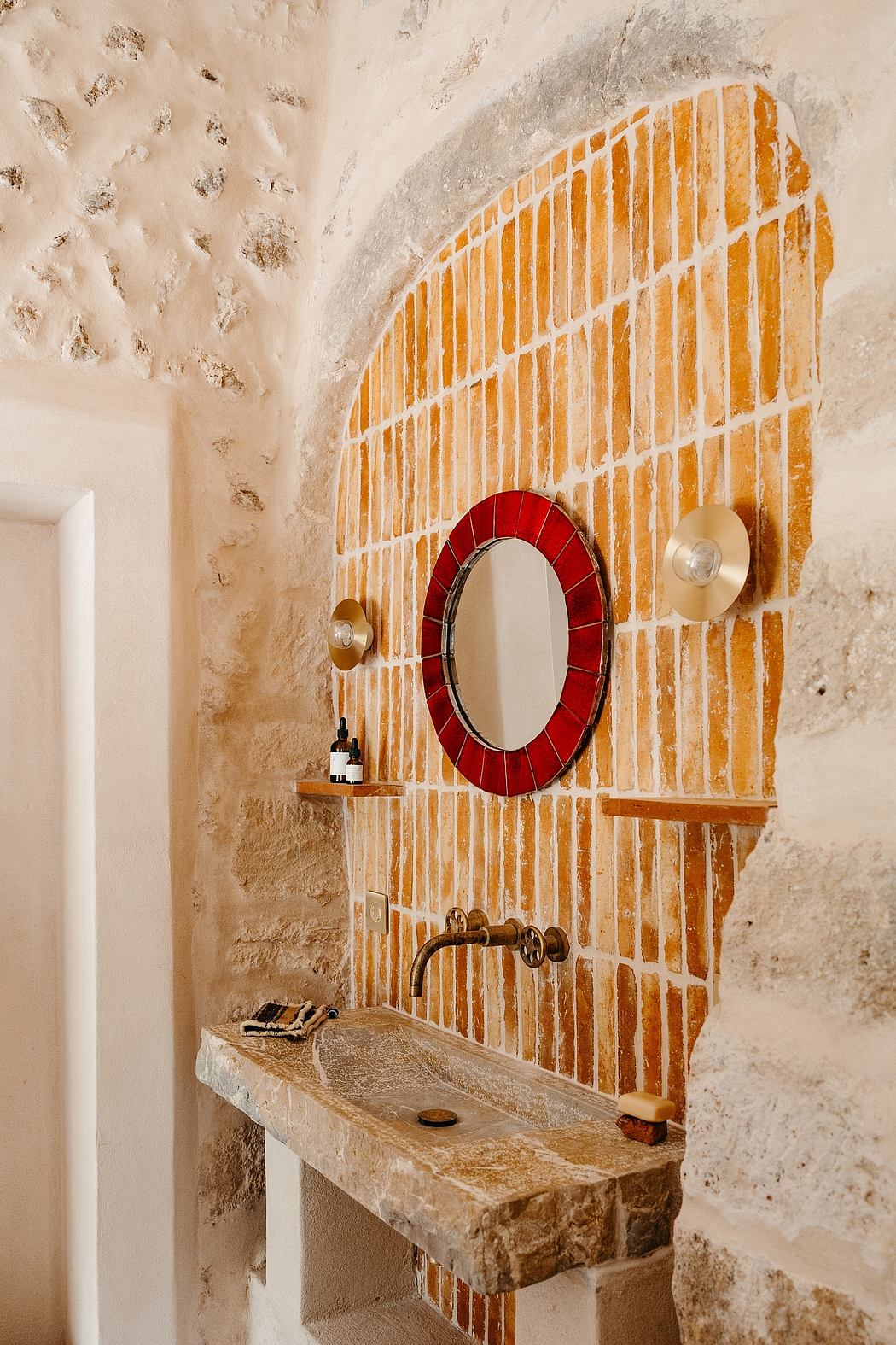 A rustic bathroom with a red mosaic-framed mirror, wooden shelves, and a stone sink.