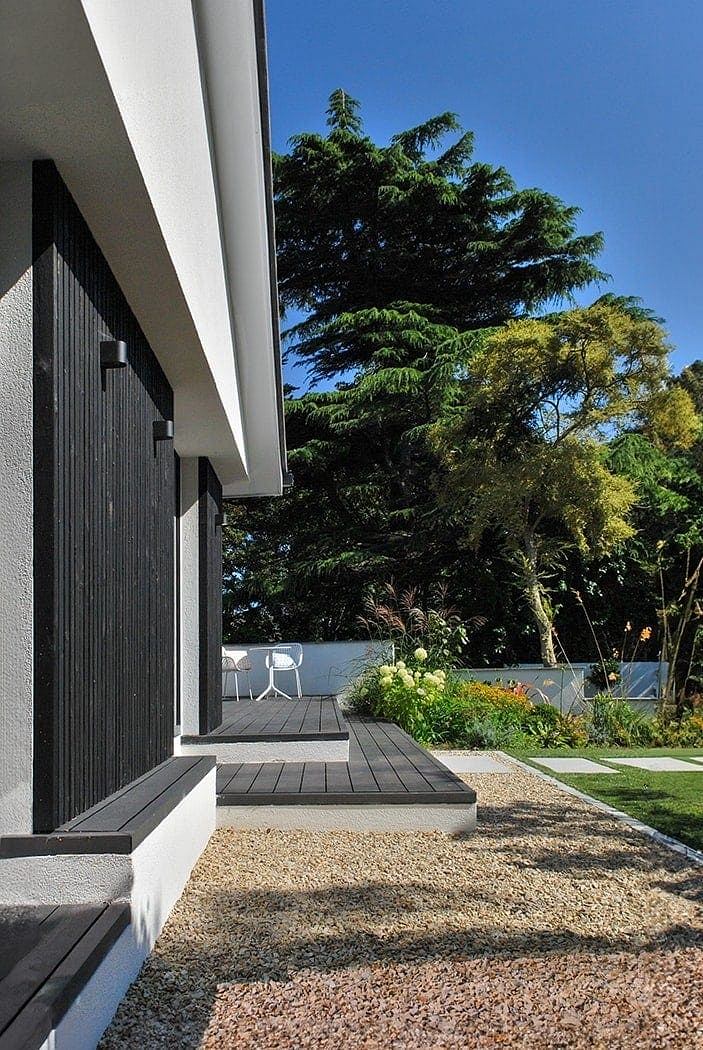 Modern home exterior with wood deck, lush greenery, and minimalist design elements.