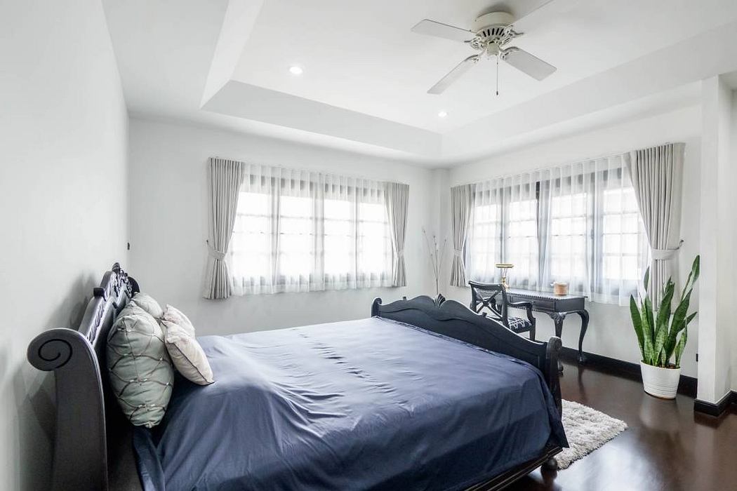 Spacious bedroom with large windows, dark furniture, and a plush bed with gray linens.