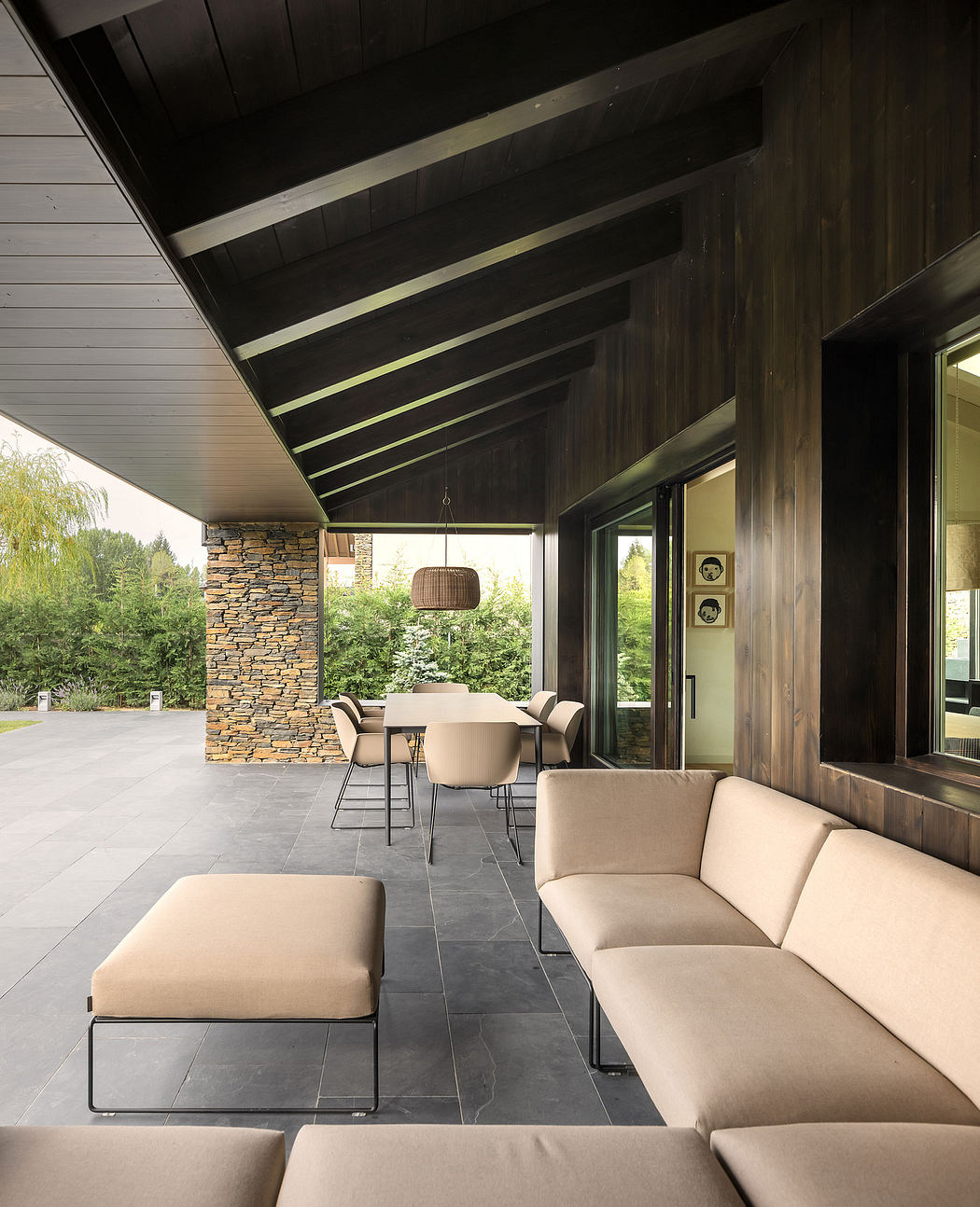 Cozy modern outdoor lounge with wooden beams, stone fireplace, and plush seating.