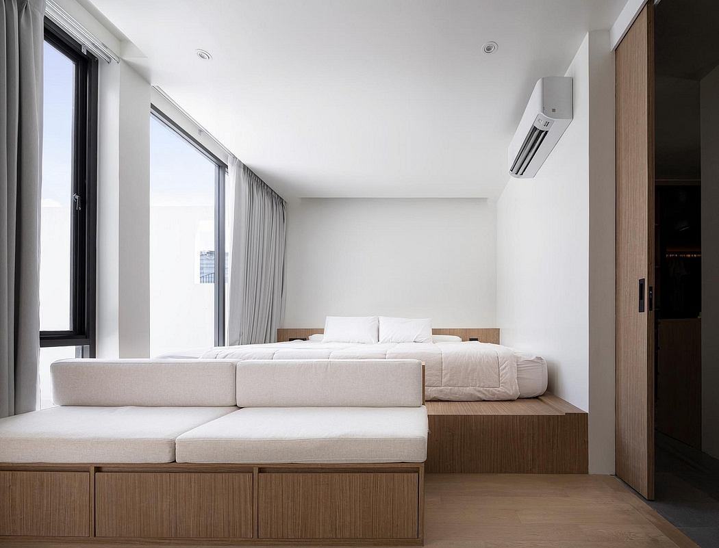 Minimalist bedroom with built-in wooden platform bed and sofa, complemented by large windows.