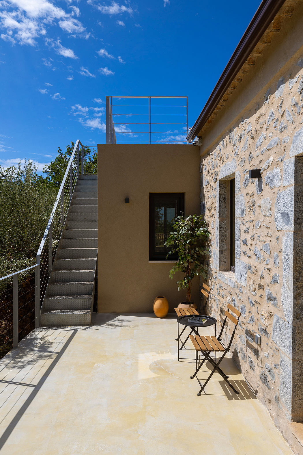 Rustic stone exterior with modern steel staircase and cozy outdoor seating area.