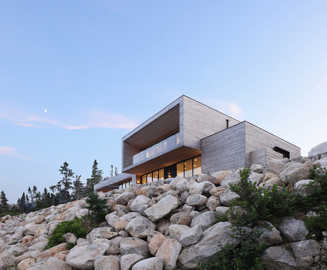 Modern, wood-clad home nestled among boulders with large windows and balcony overlooking scenic landscape.