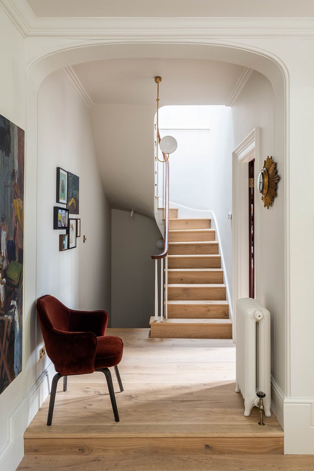 Elegant white arched entryway leads to a wood-paneled staircase and a plush red chair.