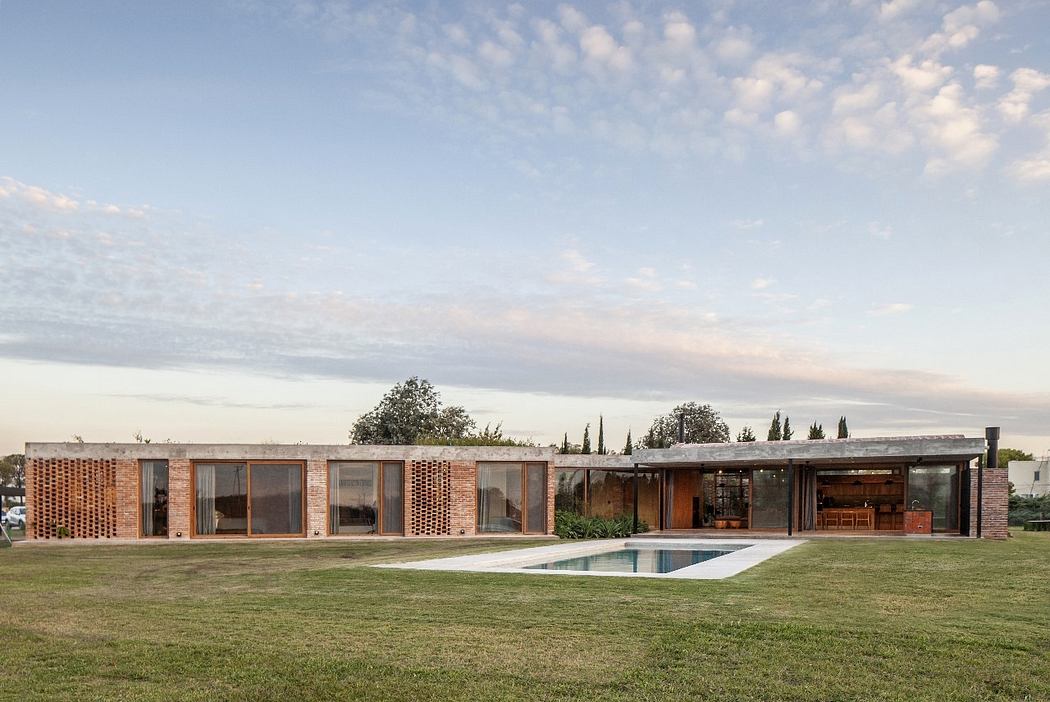 Contemporary single-story home with brick facade, glass walls, and wooden accents, surrounded by lush greenery and an inground pool.