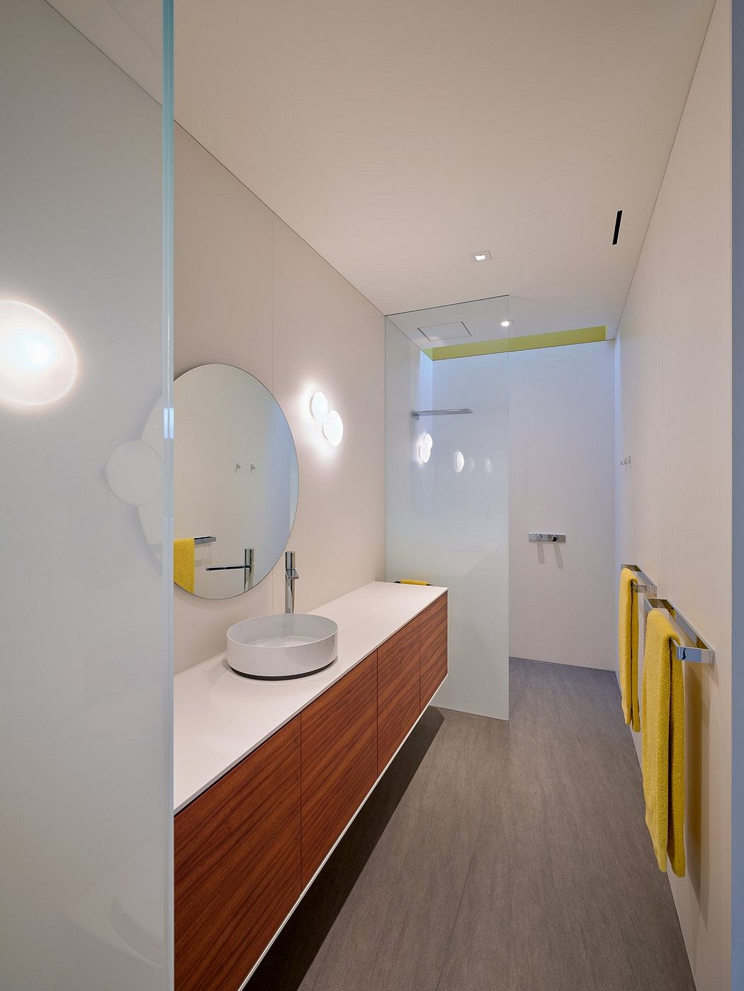 Modern bathroom with wooden vanity, round mirror, and pale yellow accents.
