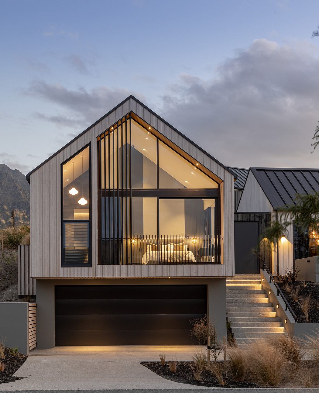 A modern, angular home with a glass-paneled gable and illuminated garage entrance.