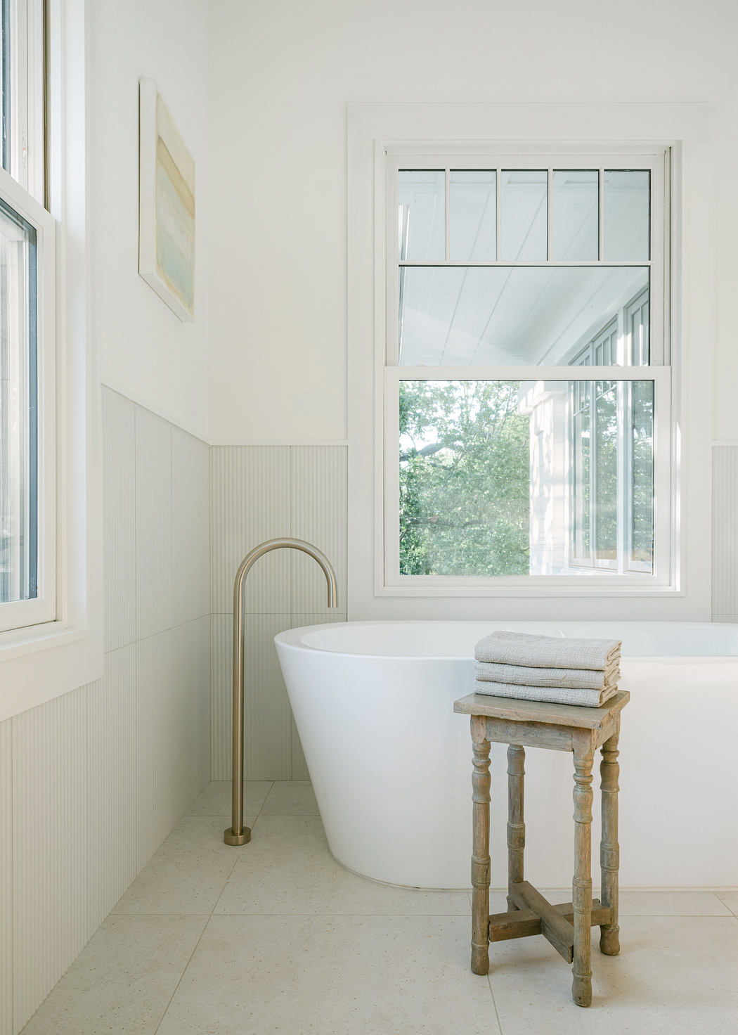 Serene bathroom with freestanding tub, wood side table, and large window overlooking greenery.