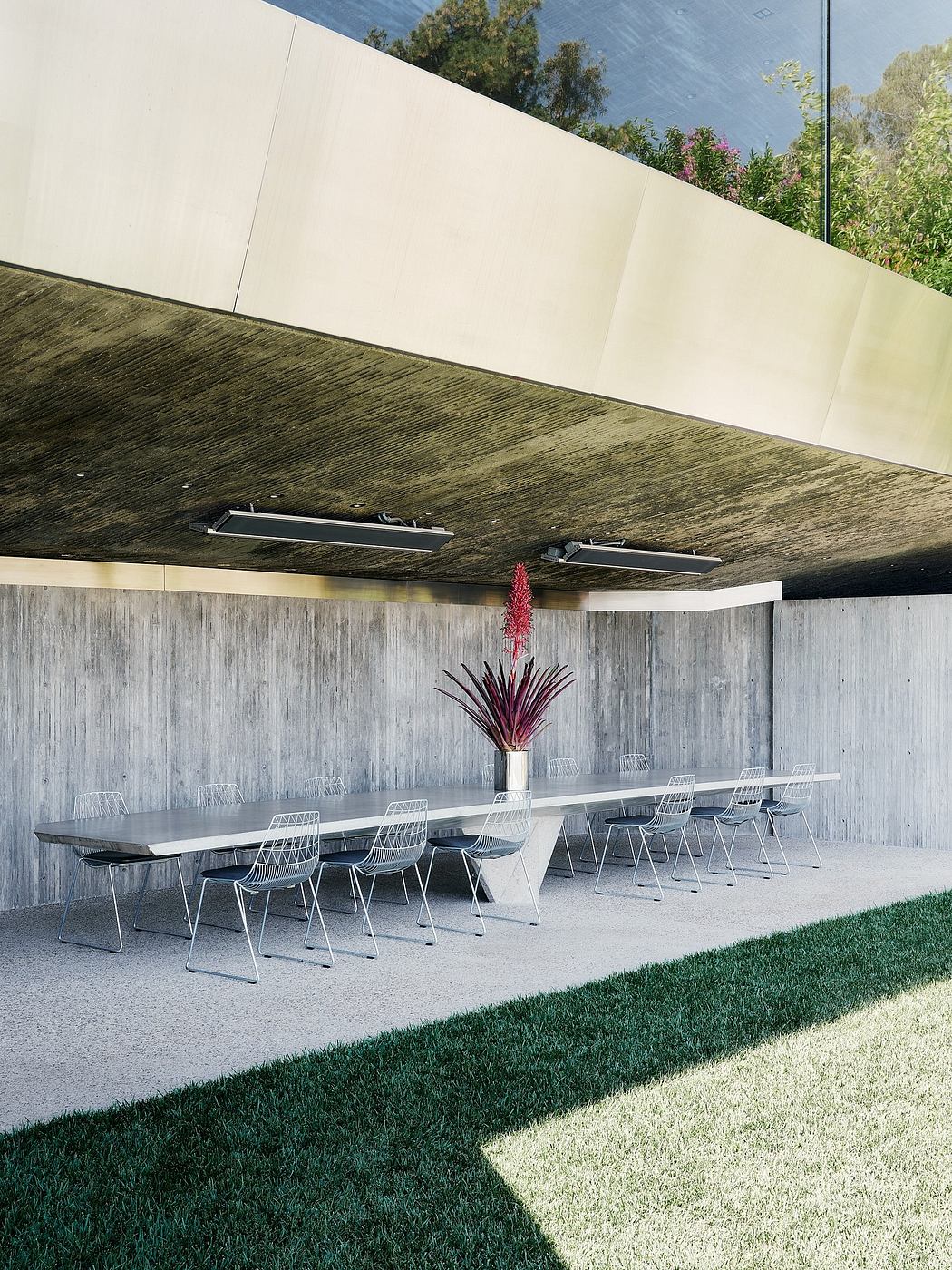 An outdoor dining area with a modern, minimalist design featuring concrete walls, metal chairs, and a floral centerpiece.