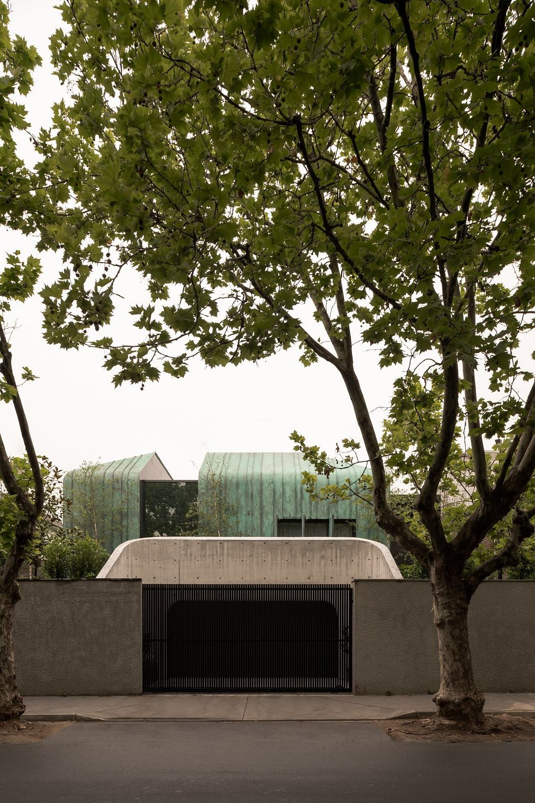 A modern, concrete structure with green copper roofs, framed by lush, leafy trees.