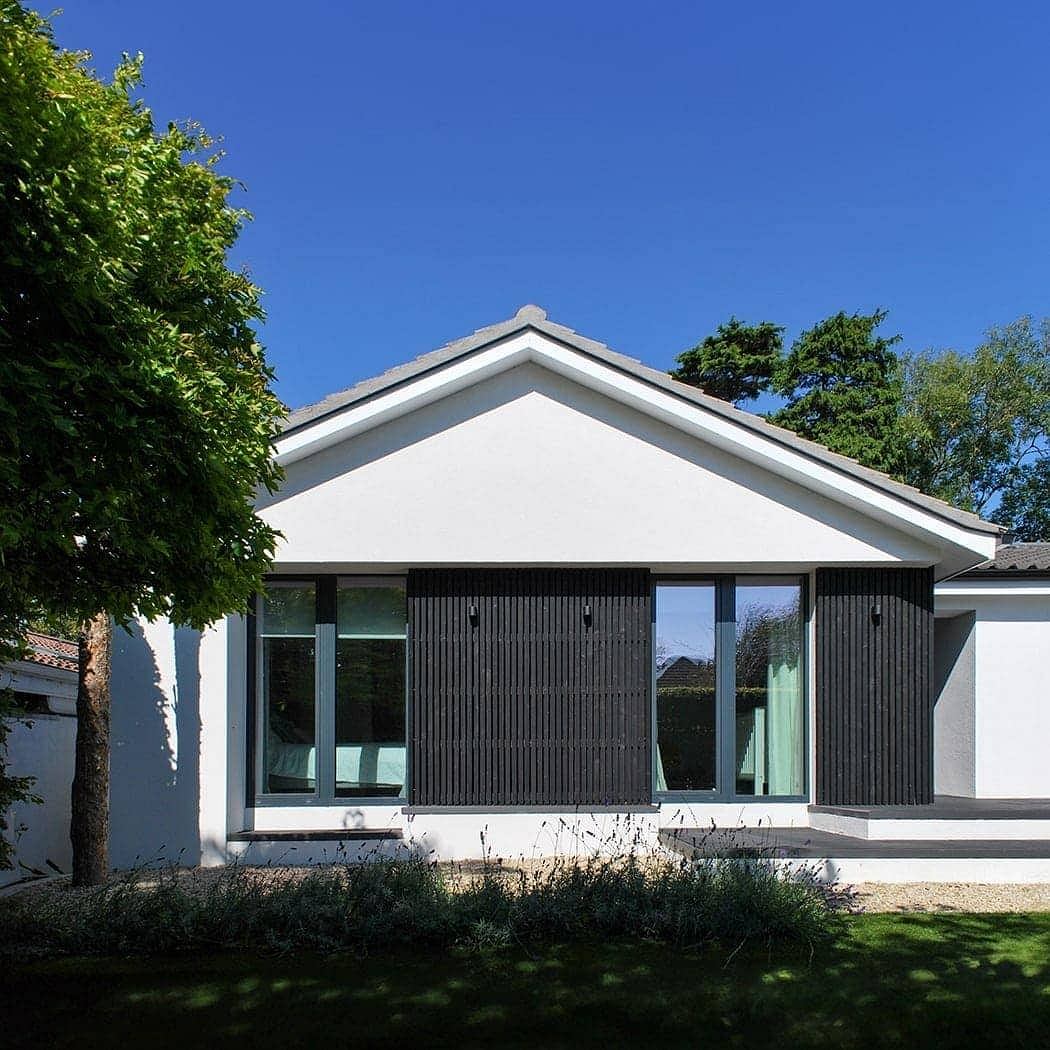 Modern single-story home with white facade, black wooden trim, and large windows.