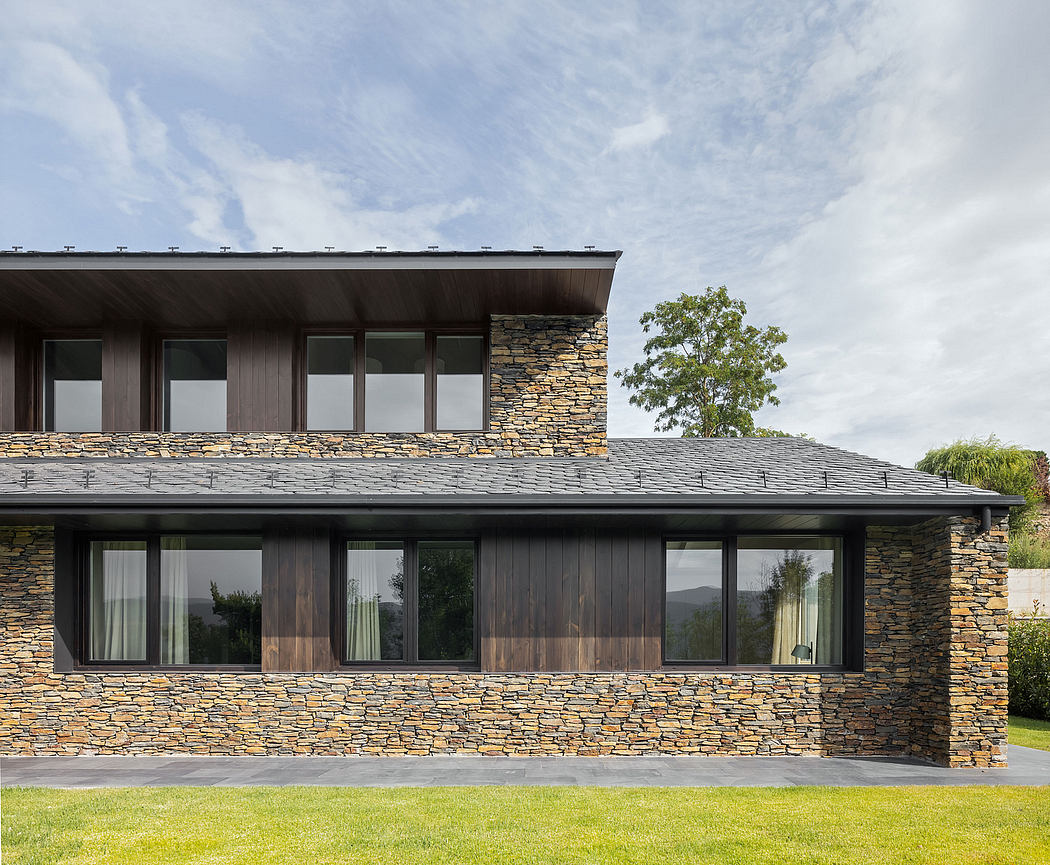 Contemporary stone and wood facade with large windows overlooking a grassy yard.