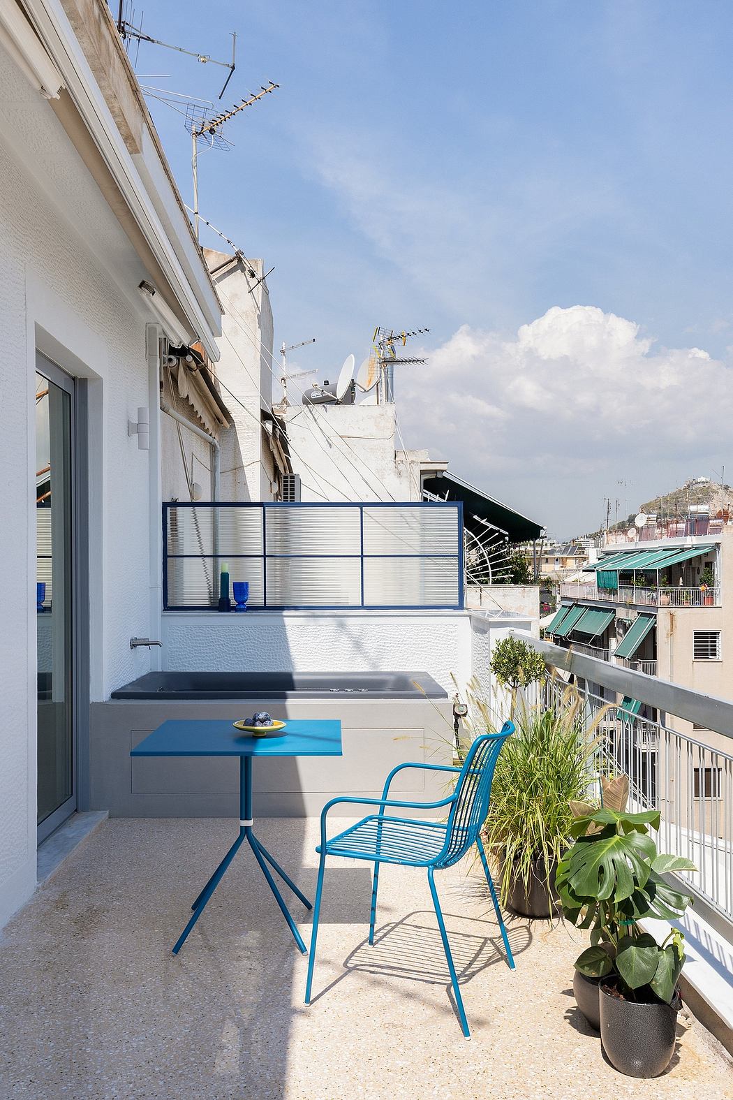 Balcony with blue metal furniture, potted plants, and an urban cityscape backdrop.