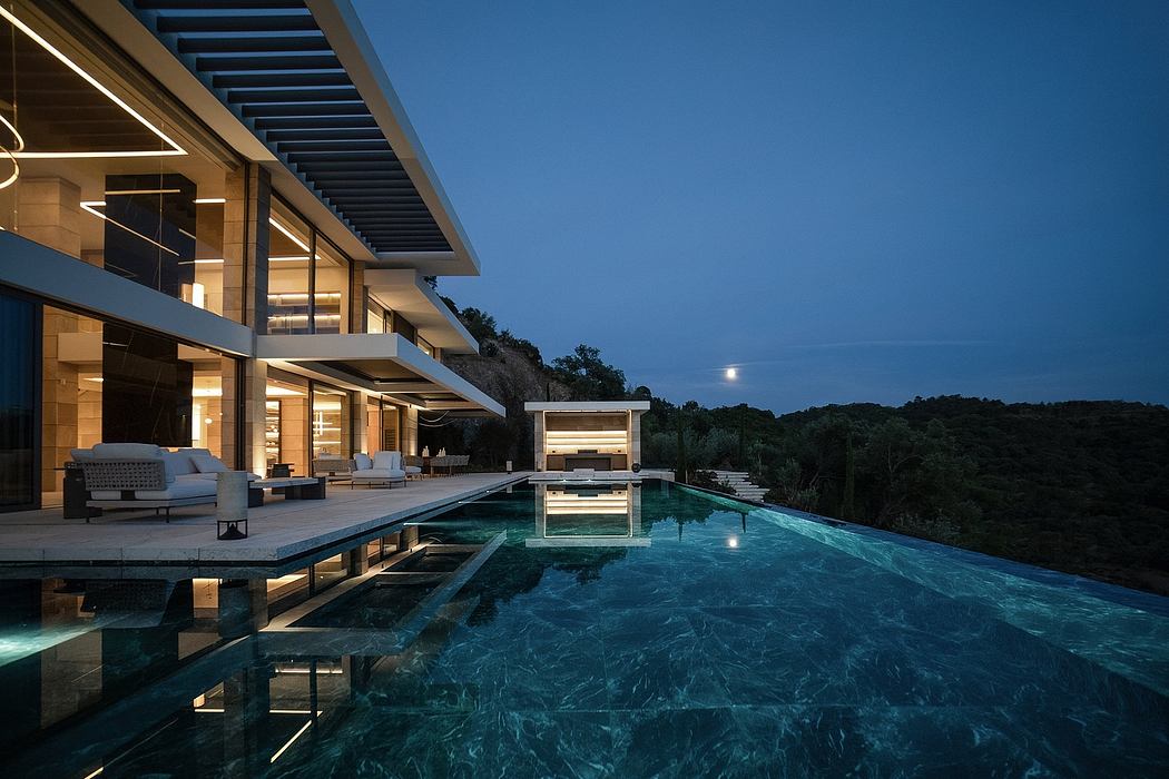 Modern, sleek outdoor space with a large pool overlooking a wooded landscape at night.