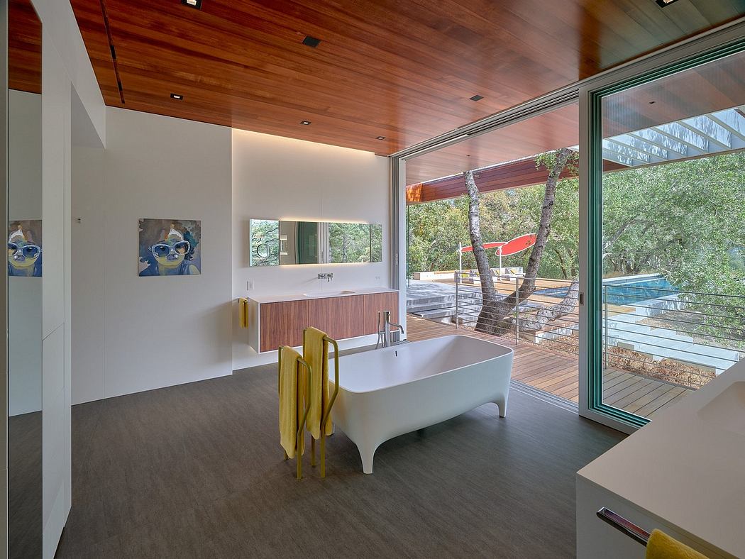 A modern bathroom with a freestanding tub, wooden ceiling, and large windows overlooking nature.