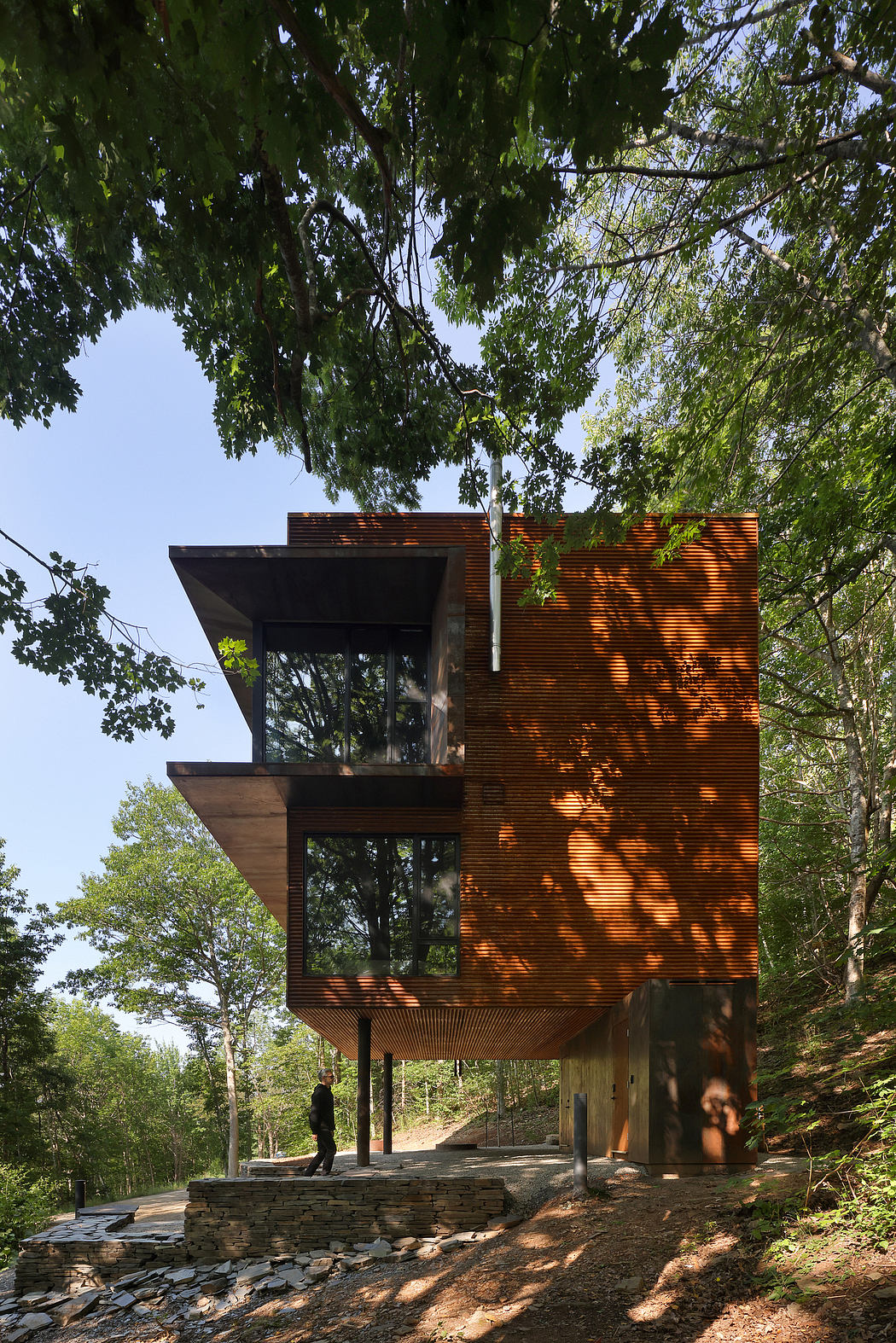 A modern, wood-clad structure with large windows in a forested landscape.