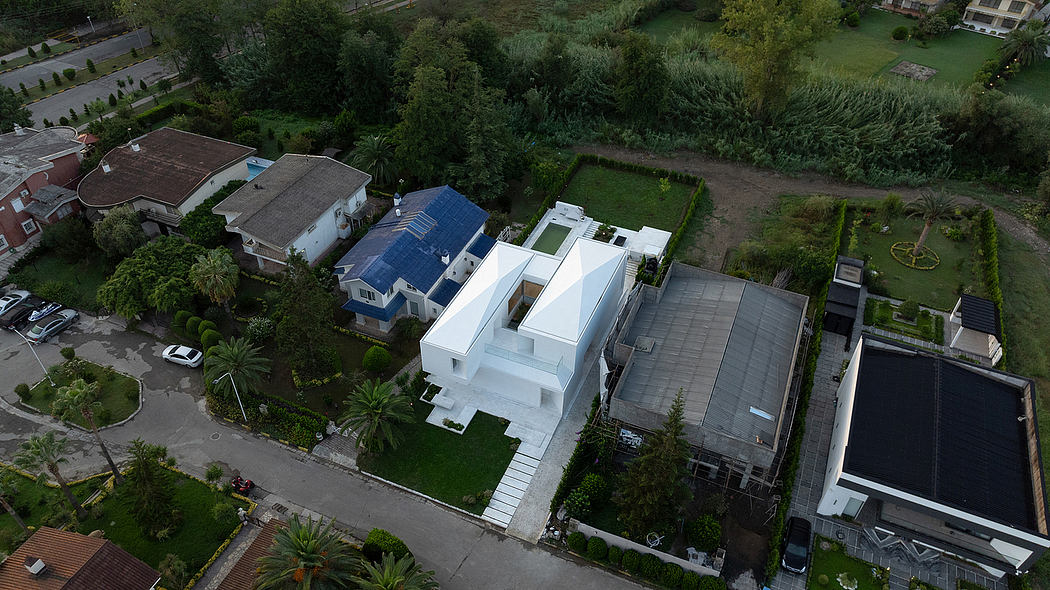 Aerial view of a contemporary, geometric white house with a lush, landscaped garden.