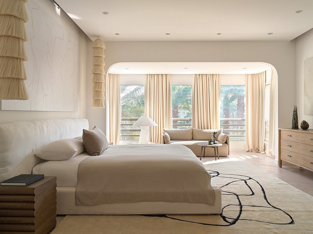 Elegant beige bedroom with arched windows, plush bedding, and cozy sitting area.