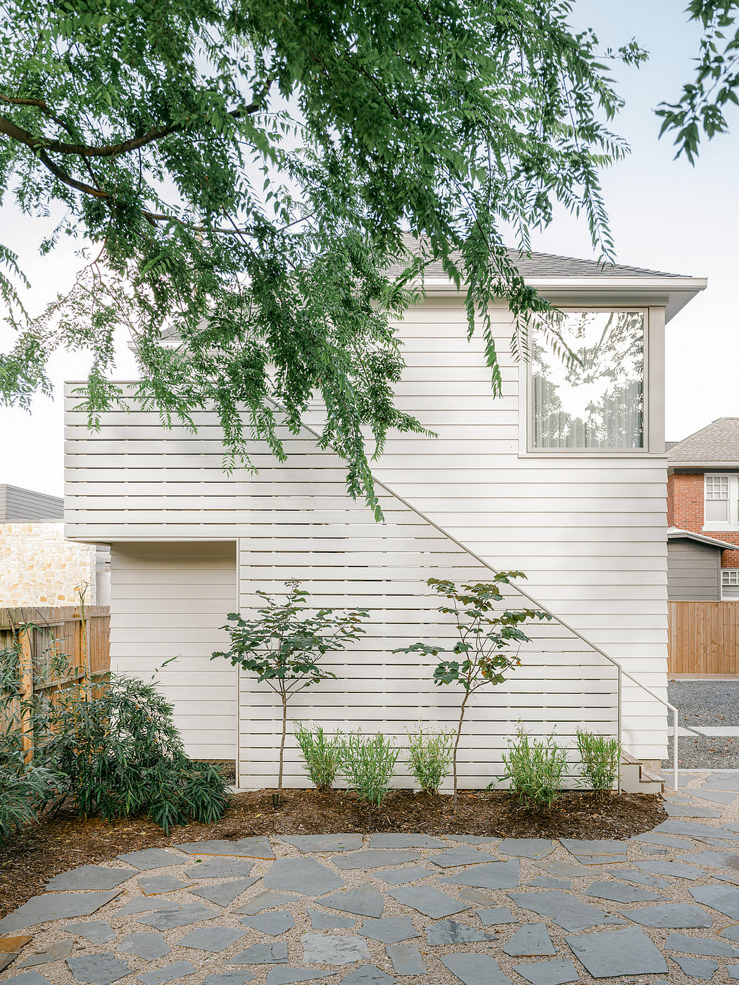 Modern, minimalist exterior with slatted wood siding, flagstone patio, and lush foliage.