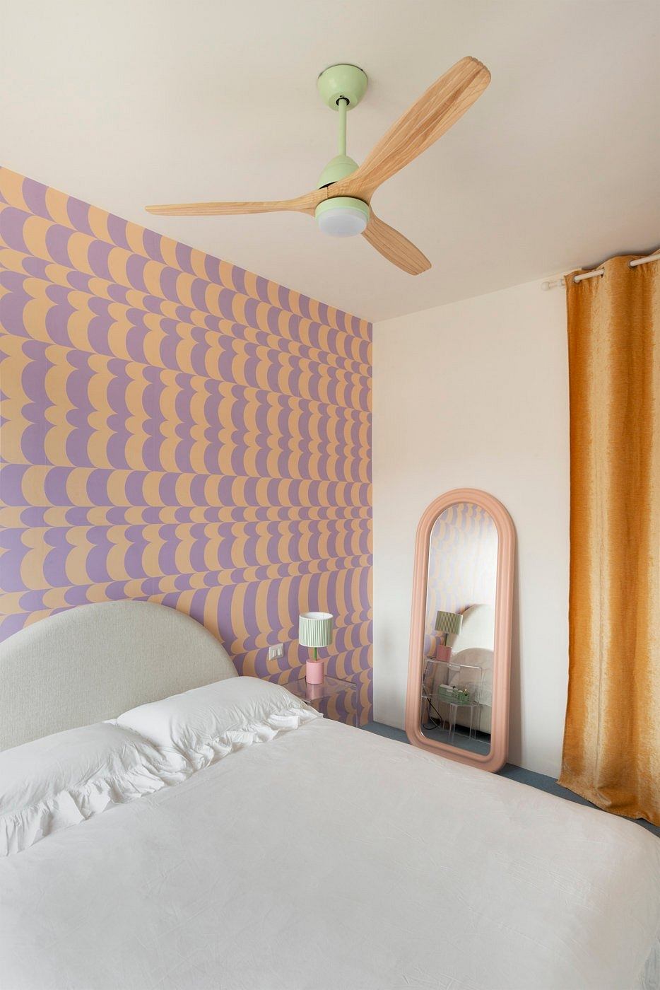 Vibrant geometric wallpaper, sleek ceiling fan, and a pink-framed mirror in a bedroom.