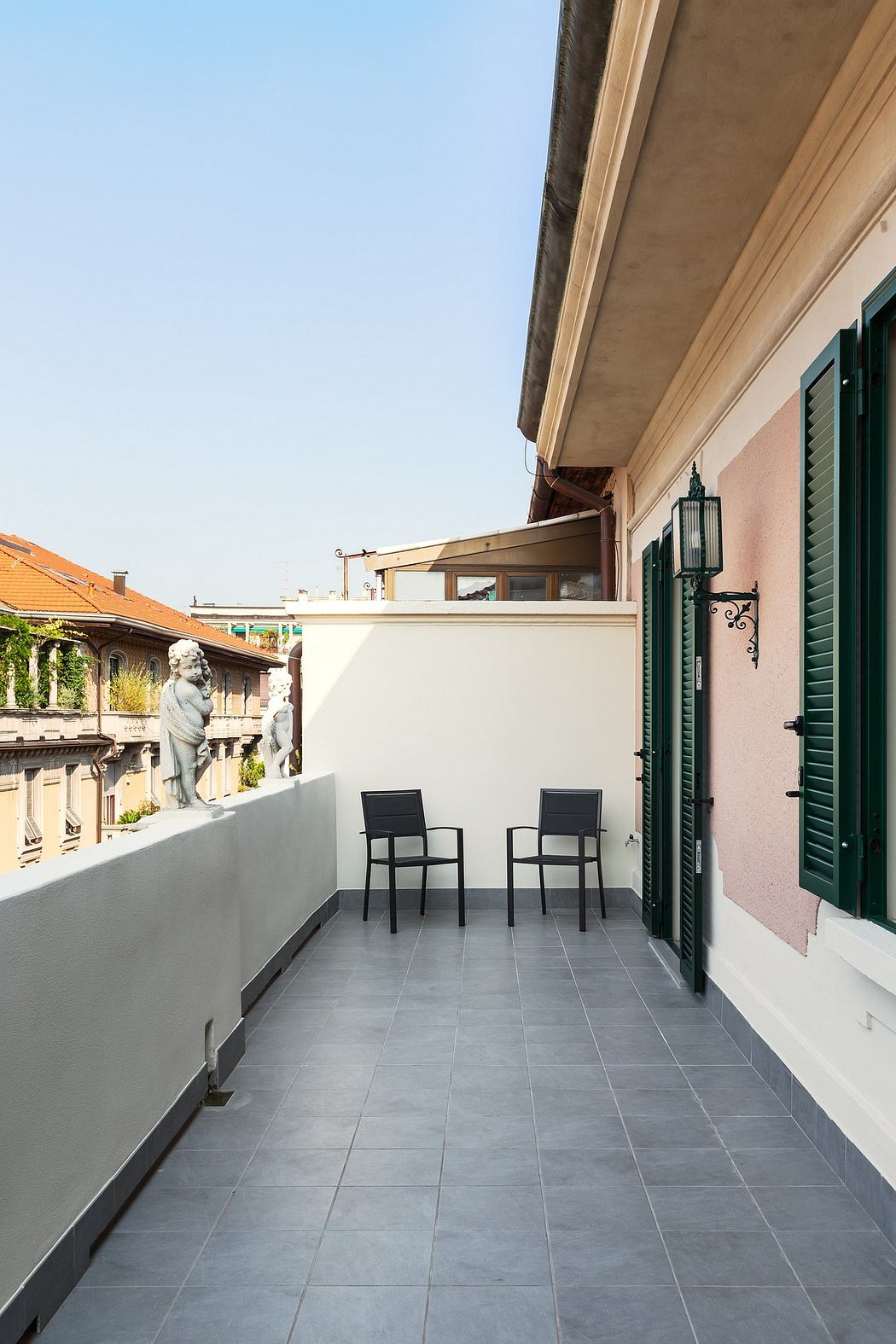 A balcony with gray tile flooring, two black chairs, and ornate architectural details.