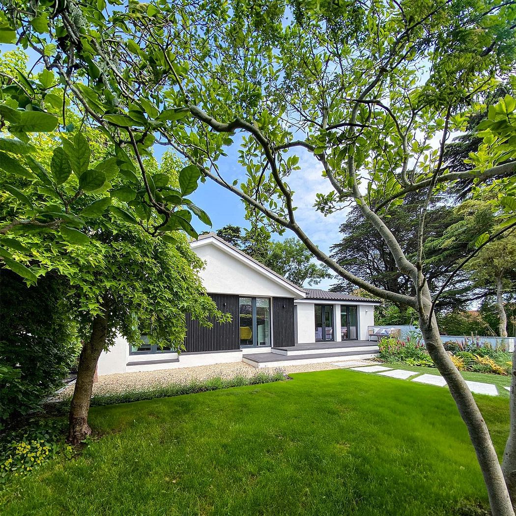 A modern, single-story home with large windows and a sleek, black exterior surrounded by lush greenery.