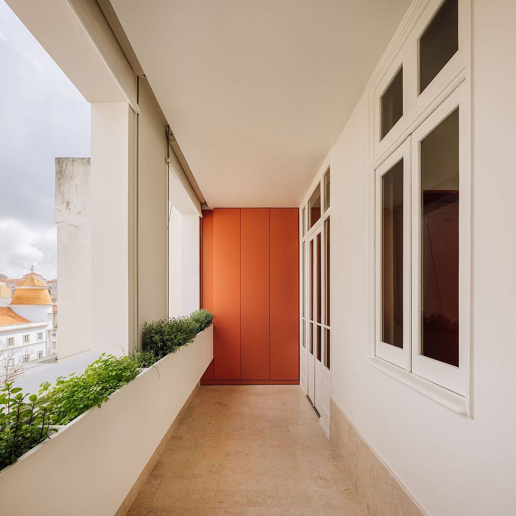 A modern balcony with white walls, a vibrant orange sliding door, and lush greenery.