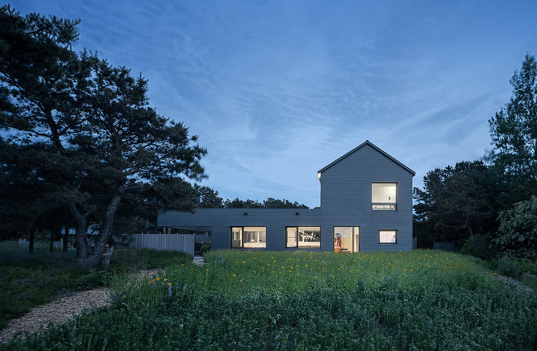 A modern home with a pitched roof and numerous windows nestled in a lush, grassy landscape.