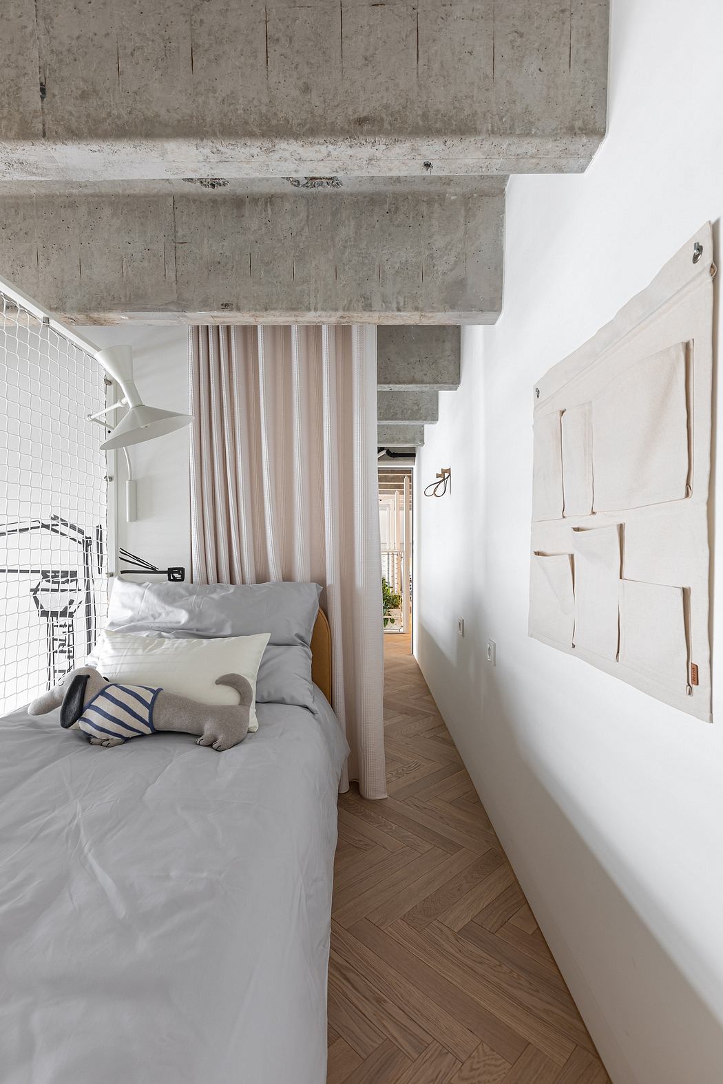 A minimalist bedroom with concrete ceiling, white walls, and a herringbone wood floor.