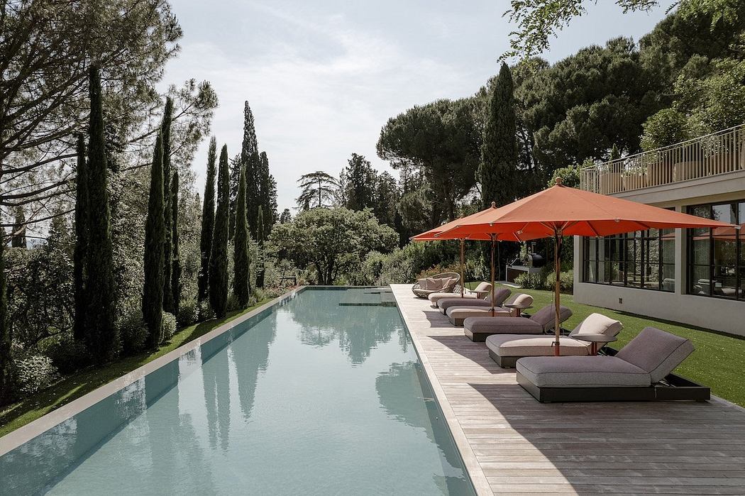A luxurious outdoor pool area with a wooden deck, sun loungers, and red umbrellas in a lush, forested setting.
