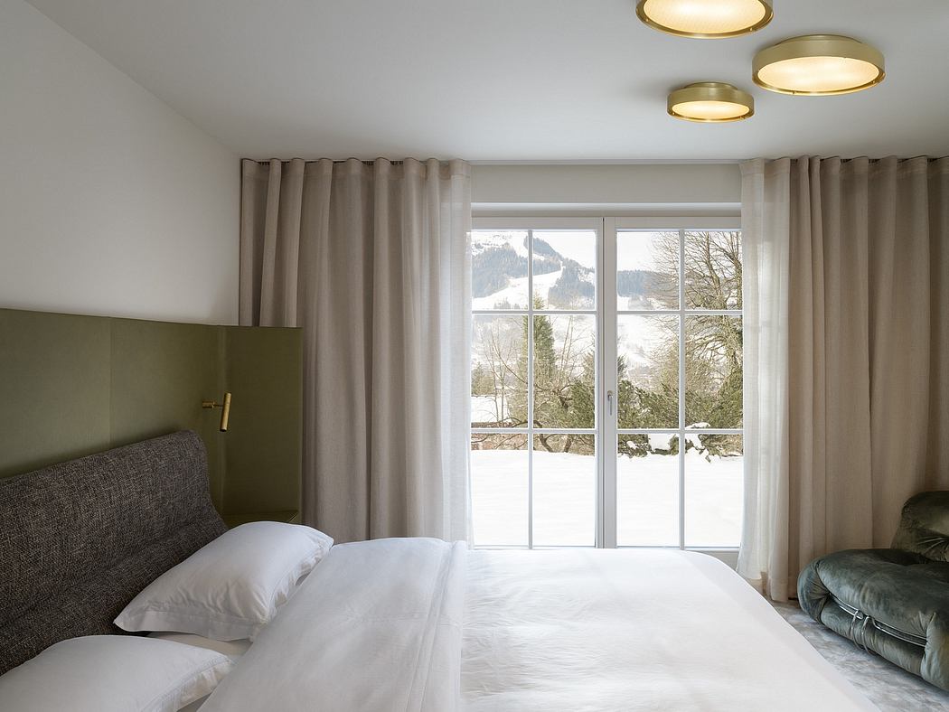 A modern, minimalist bedroom with large windows overlooking a snowy landscape, recessed lighting, and plush furnishings.