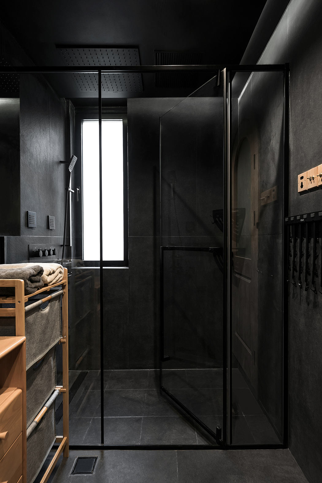 A minimalist bathroom with sleek black walls, a wooden vanity, and a large glass shower enclosure.