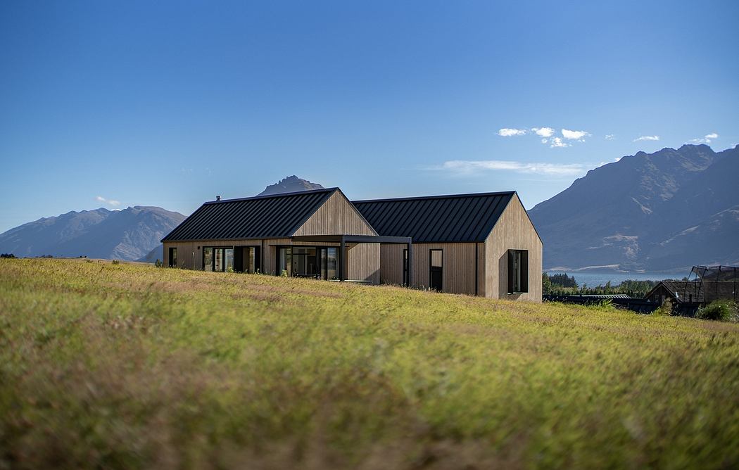 A modern, wooden-clad house with a distinctive gable roof, nestled in scenic mountains.