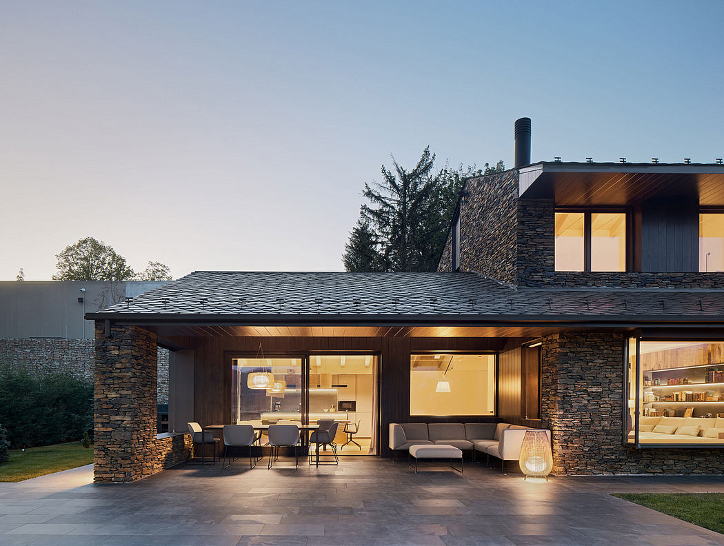Stunning modern exterior with stone walls, slanted roofs, and expansive windows showcasing the interior.