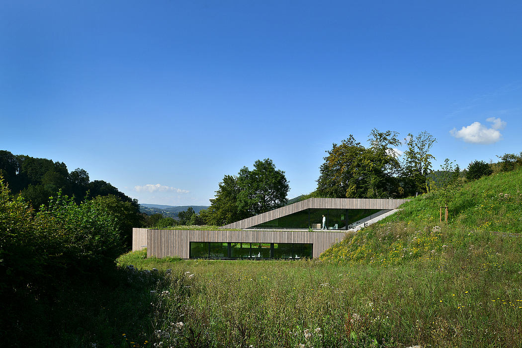 Wooden building set into a grassy hill, with large windows overlooking the surrounding landscape.