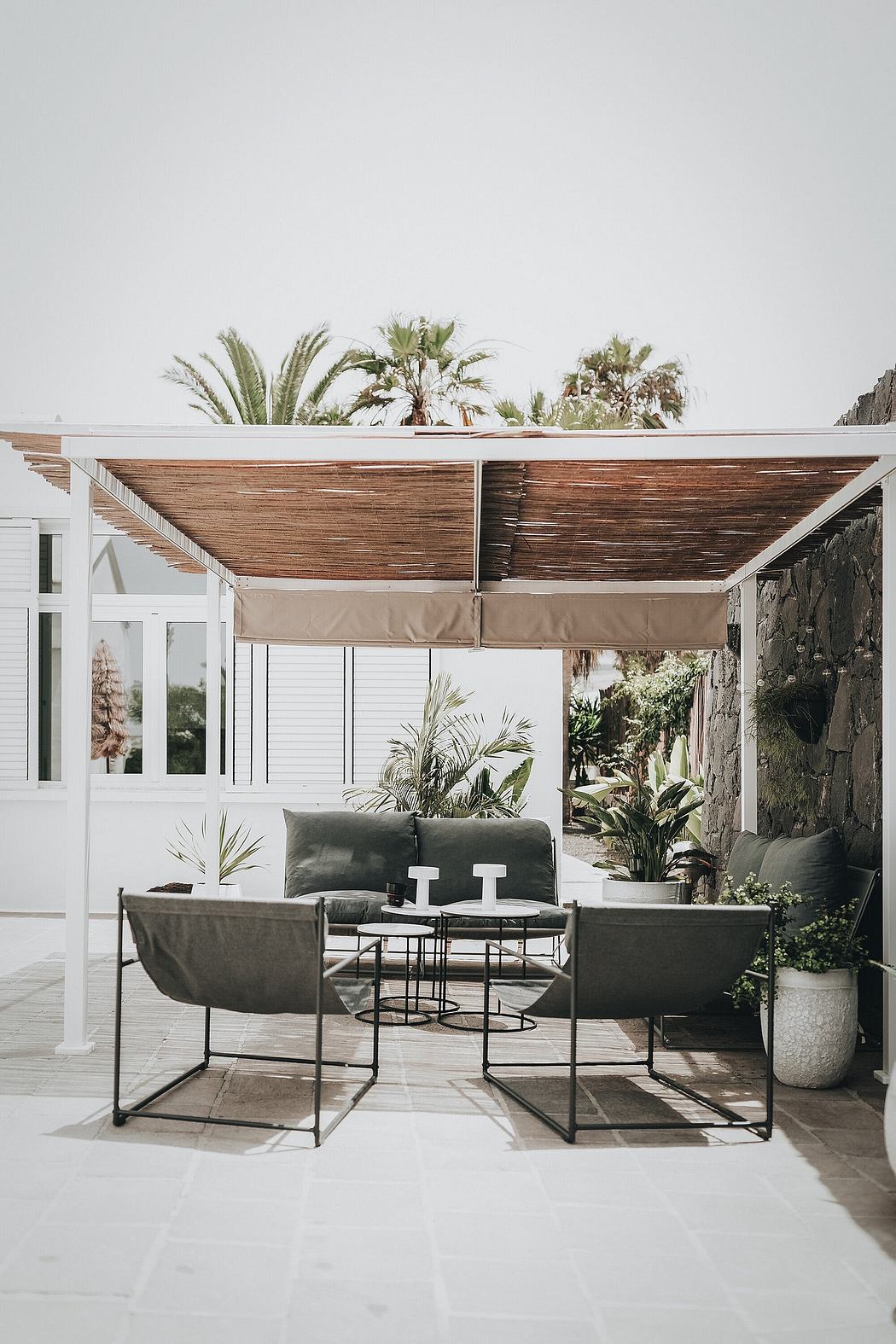 Covered outdoor patio with modern, minimalist furniture and lush greenery.