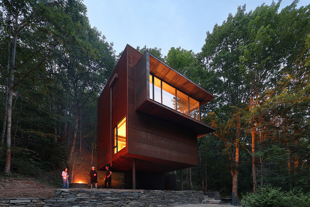 Striking modern cabin with wooden cladding, glass walls, and elevated platform in forest setting.