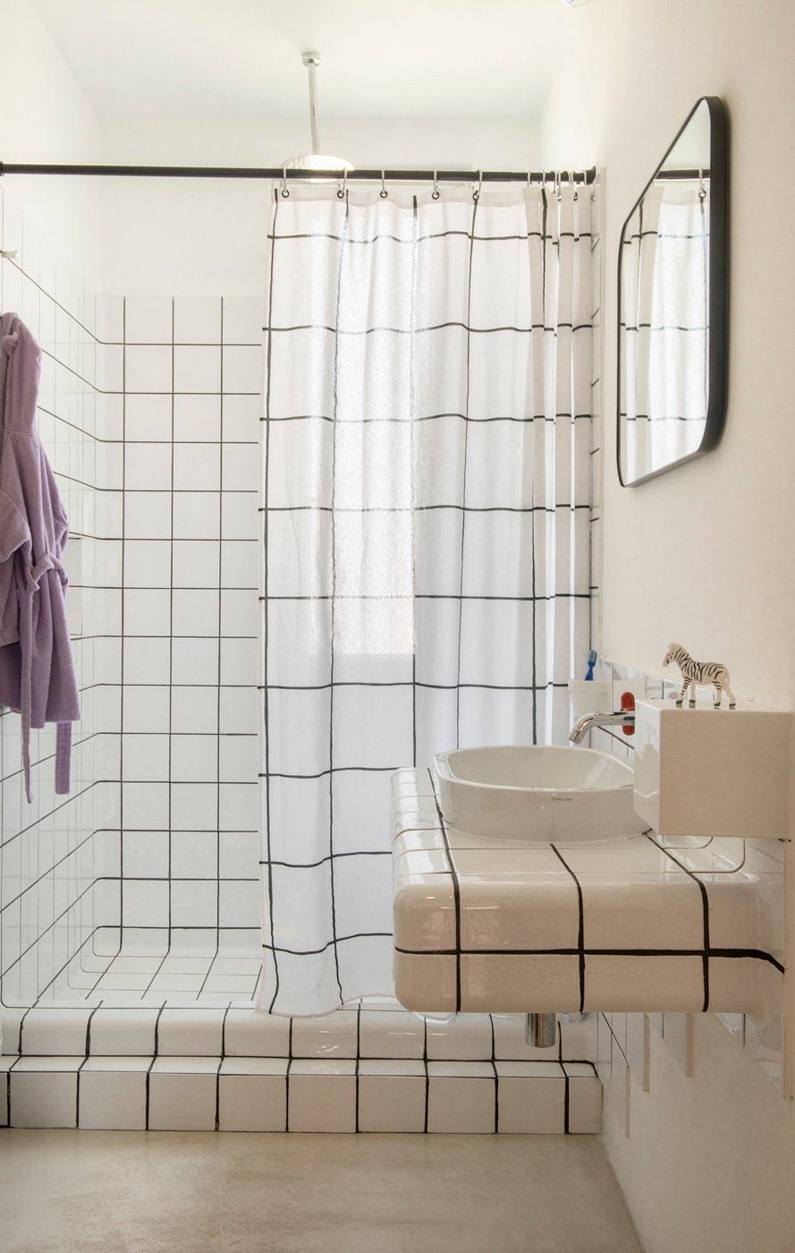 A minimalist bathroom with a grid-patterned tiled floor, a vessel sink, and a striped curtain.