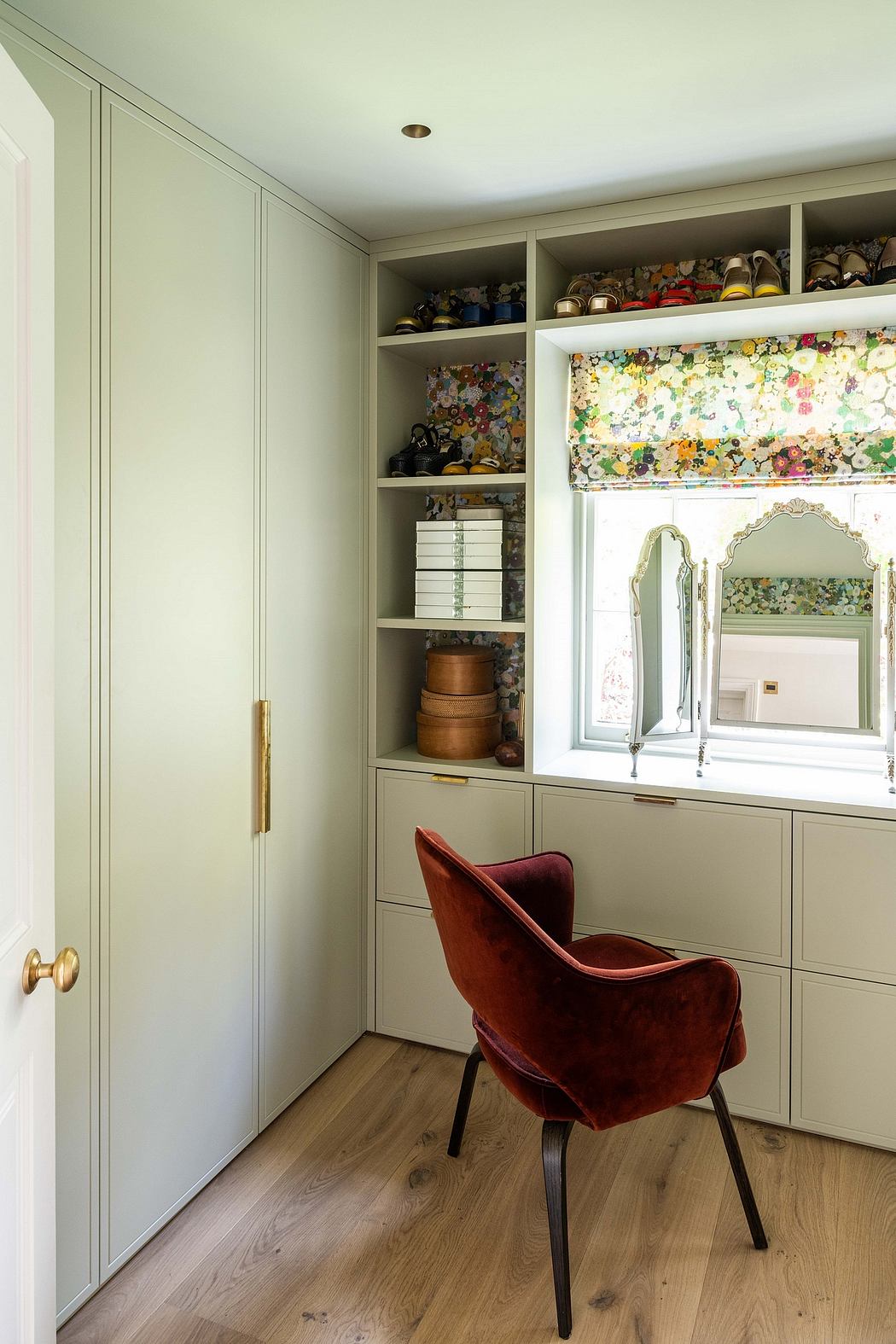 A cozy, well-designed room with built-in cabinetry, a floral window shade, and a plush red chair.