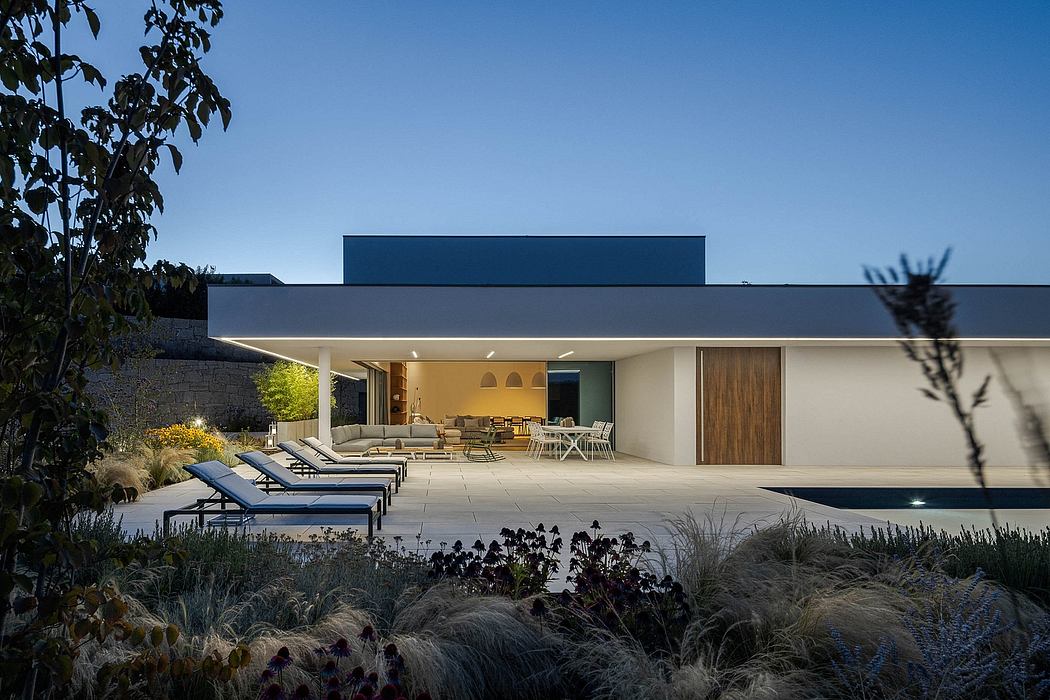 A modern, sleek home with a patio, pool, and lush landscaping under a night sky.