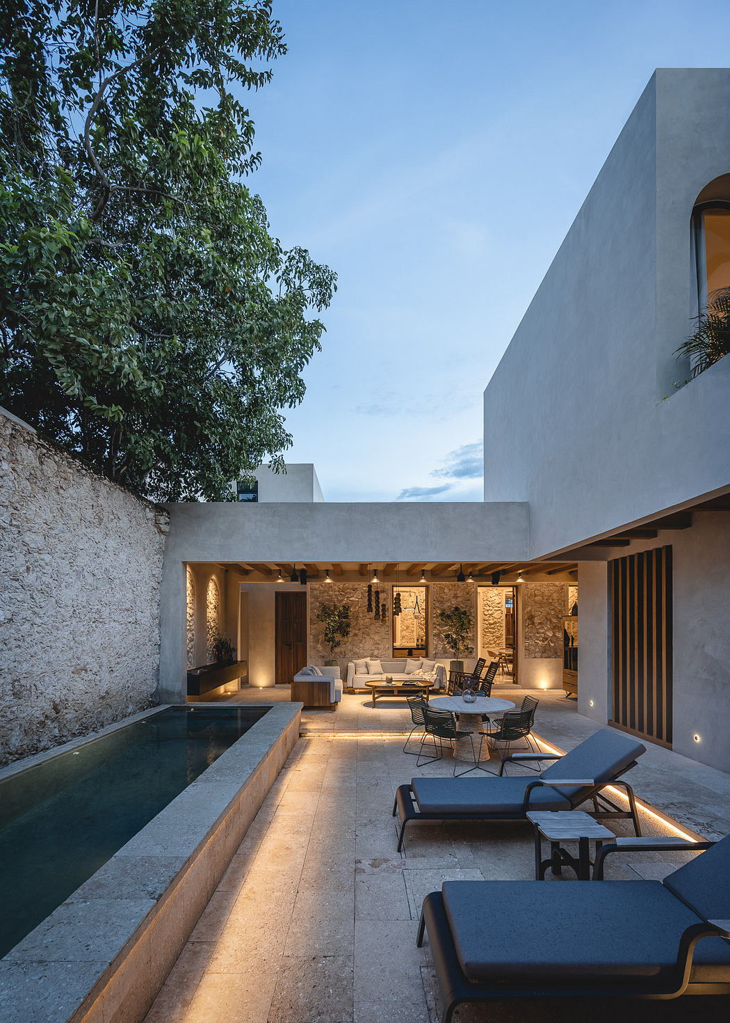 Sleek, modern courtyard with a pool, seating areas, and warm lighting accenting stone walls.