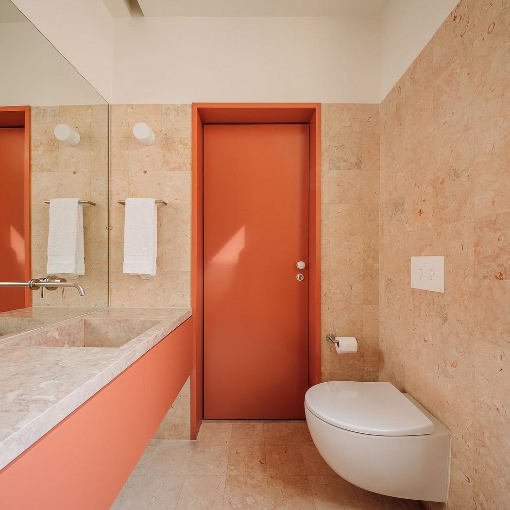 Spacious bathroom with minimalist design, warm-toned marble accents, and a vibrant orange door.