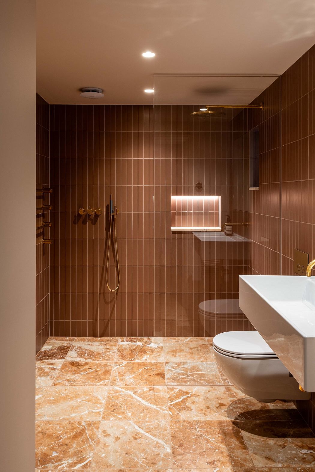 Warm-toned bathroom with brown tiled walls, marble floors, and modern fixtures.