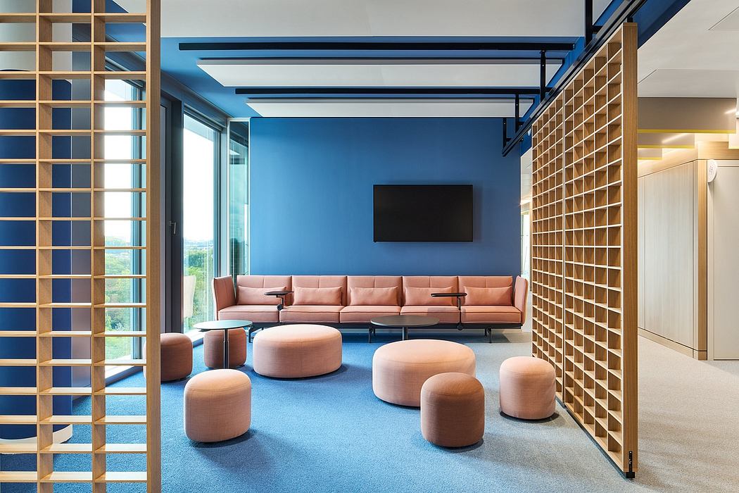 A modern lounge area with blue walls, wooden accents, and plush pink seating.