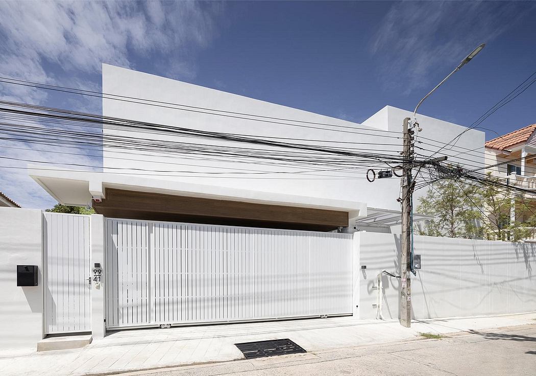 Modern white building with wooden roof overhang, metal gate, and power lines overhead.