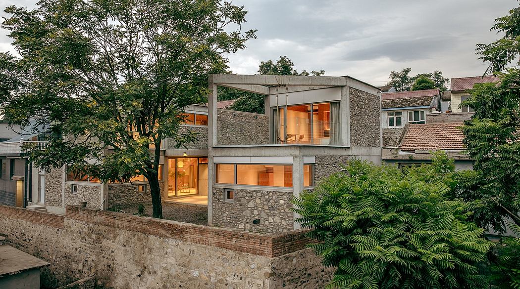 A modern stone and concrete building with large windows overlooking lush greenery.
