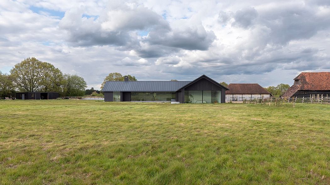 Modern farmhouse-style building with large windows overlooking a grassy field and wooded area.