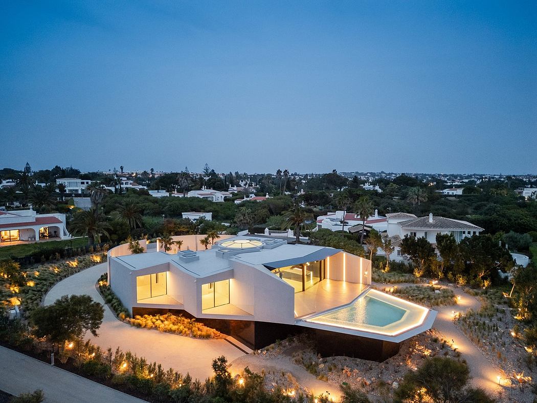 A modern, angular villa with a pool nestled among landscaped gardens, illuminated at night.
