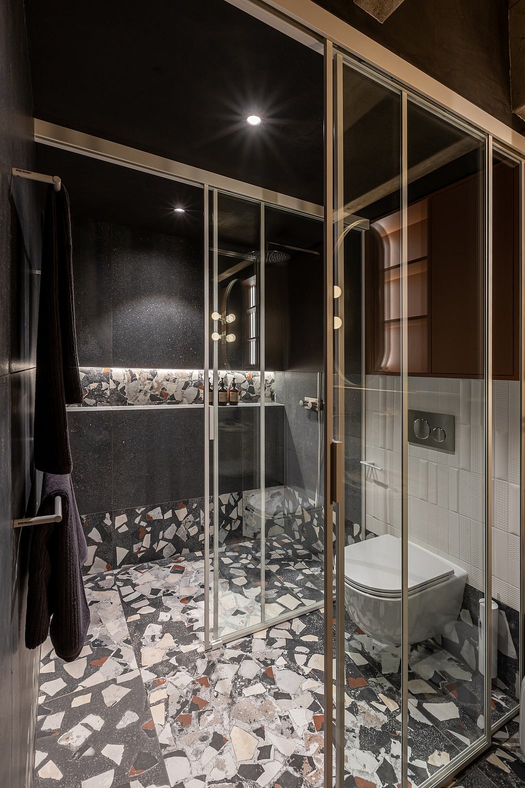 Striking modern bathroom featuring black and white terrazzo tiles and glass shower enclosure.